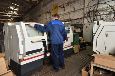 Mavi iş elbisesi işçisi, Cnc makinesini çalıştırıyor, süreci denetliyor. Cnc makinesiyle fabrikada çalışan adam..