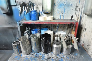 Boya odasındaki masa boyayla boyandı. Masanın üzerinde su ve boya dolu sprey tabancalar ve kaplar var. Boya odası ve fabrika atölyesi
