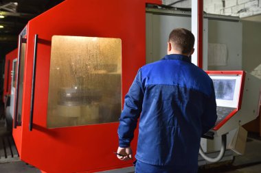 Mavi iş elbisesi işçisi, Cnc makinesini çalıştırıyor, süreci denetliyor. Cnc makinesiyle fabrikada çalışan adam..