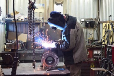 Fabrikadaki demir sehpanın ve kaynak makinesiyle kaynak yapan işçinin kapakçığı. Kıvılcımlar uçuşuyor