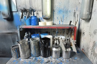 Boya odasındaki masa boyayla boyandı. Masanın üzerinde su ve boya dolu sprey tabancalar ve kaplar var. Boya odası ve fabrika atölyesi