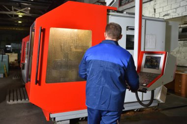 Mavi iş elbisesi işçisi, Cnc makinesini çalıştırıyor, süreci denetliyor. Cnc makinesiyle fabrikada çalışan adam..