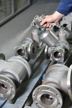 Özel odadaki fabrikada çalışan bir işçi sprey tabancanın kapakçıklarını boyuyor. Gri renkli boyama valfleri, eller kapalı..