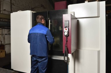 Mavi iş elbisesi işçisi, Cnc makinesini çalıştırıyor, süreci denetliyor. Cnc makinesiyle fabrikada çalışan adam..