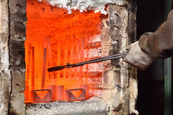 İşçi, metali sertleştirmek için elektrikli fırından maşayla ısıtılmış parçaları çıkarıyor. Valf imalat tesisinde ağır sanayide yüksek sıcaklıkla çalışmak, yakın çekim