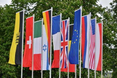 Almanya 'nın Baden-Baden kentindeki parktaki farklı ülkelerin bayrakları ağaçların arka planına karşı. Almanya Cumhuriyeti, İsviçre, Fransa, Amerika, İngiltere, İsrail Bayrakları
