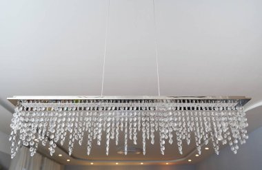 Dikdörtgen şeklinde güzel bir avize. Pencere perdesinin arkasında ışık saçan kristaller asılı.