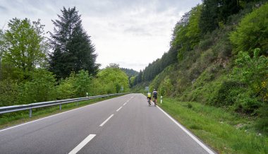 Dönüşleri olan bir ormanın içinden geçen otoyol ve iki bisikletçi ormandan geçiyor. Schwarzwald Orman Yolu ve Bisikletçiler