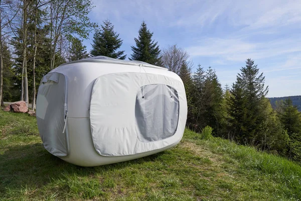 Unusual modern tent in the form of a cube for outdoor recreation or sleep, set on the mountainside next to the forest on green grass. Sleeping tent