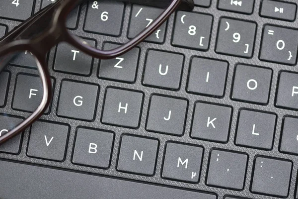 Black-rimmed eyeglasses lie on the laptop keyboard as a symbol of vision loss and fatigue. Close-up