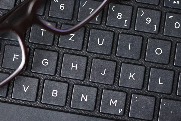 Black-rimmed eyeglasses lie on the laptop keyboard as a symbol of vision loss and fatigue. Close-up