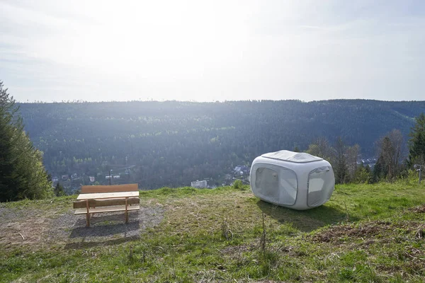 Unusual modern tent in the form of a cube for outdoor recreation or sleep, set on the mountainside next to the forest on green grass. Sleeping tent