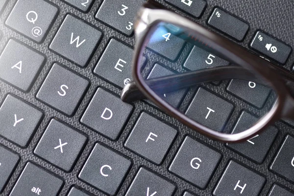 Black-rimmed eyeglasses lie on the laptop keyboard as a symbol of vision loss and fatigue. Close-up