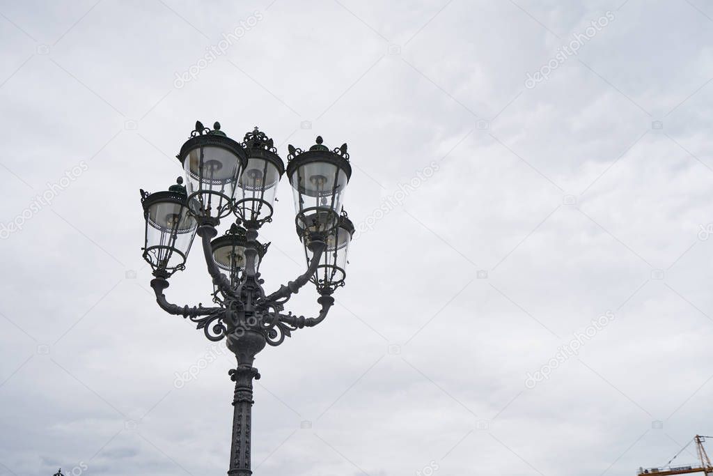Beautiful classic iron lamppost of six lamps with diode bulbs against a cloudy sky in a European city