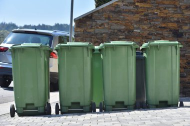 Yeşil çöp tenekeleri duvarın önünde duruyor. Çöpleri ayırmak için çöp konteynırları