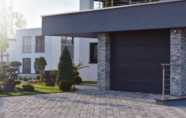 Almanya 'daki bahçe bitkilerinin yanında otomatik kapısı olan modern bir Avrupa evinin garajı.