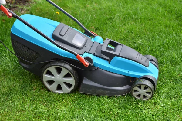 Electric lawn mower mows a bright green overgrown lawn, close-up