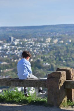 Pforzheim, Almanya - 21 Nisan 2019: Üzgün bir çocuk kentin arka planında, bankta oturuyor. Yalnızlık ve kırgınlık kavramı.