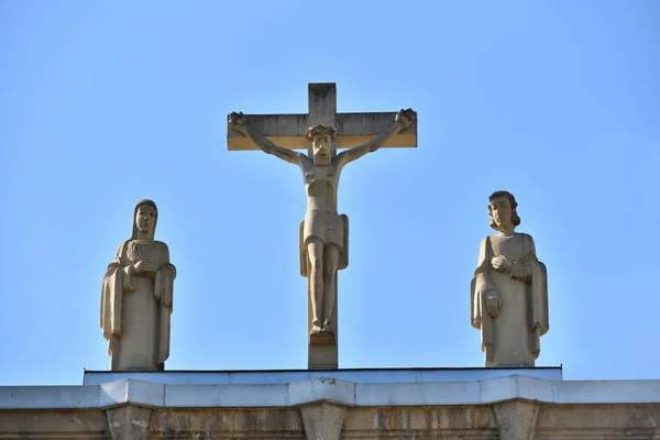 Stone statue with crucified Jesus against the blue sky on the roof of the church Heart of Jesus in the European city of Pforzheim, Germany