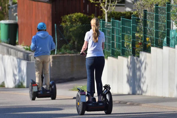 Egy bukósisak nélküli nő és egy férfi robogózik az utcán, visszapillantással. Technológia és lustaság — Stock Fotó