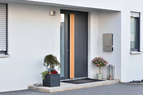 Un grande vaso grigio con un cespuglio verde di fronte all'ingresso della casa accanto alla porta grigio anteriore. — Foto Stock