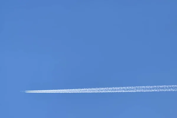 Een passagiersvliegtuig vliegt hoog in de lucht en laat een wit spoor achter tegen de blauwe lucht. Tekstruimte — Stockfoto