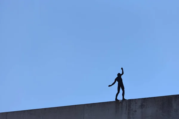 Silhouette artificial de un hombre sobre el fondo de un cielo azul que se sitúa peligrosamente en el borde de un equilibrio de edificios. Espacio de texto. El concepto de riesgo y algo peligroso — Foto de Stock