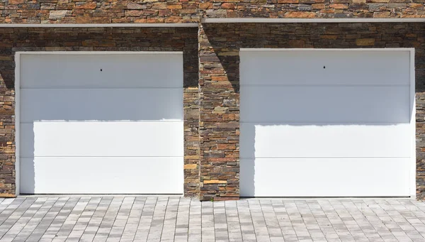 Two white automatic gates to a garage on a decorative brick wall