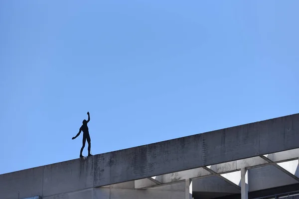 Künstliche Silhouette eines Mannes vor dem Hintergrund eines blauen Himmels, der gefährlich am Rande eines balancierenden Gebäudes steht. Textraum. Der Begriff Risiko und etwas Gefährliches — Stockfoto