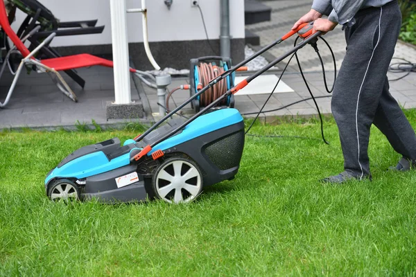 En man klipper gräsmattan i sin trädgård med en elektrisk gräsklippare, närbild — Stockfoto