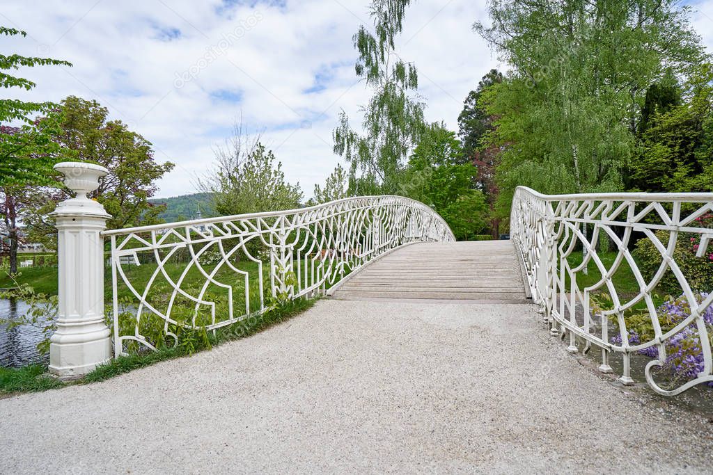 A beautiful white forged iron bridge and its railing in a public park in the European city of Baden Baden. Landscape with a bridge overlooking a green park