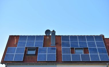 Avrupa 'da kiremitleri olan bir evin çatısına mavi gökyüzünün arka planına güneş panelleri yerleştirildi.
