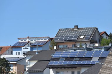 Güneş panelleri ve mavi gökyüzü olan birkaç çatı. Çatılarda fayanslı güneş panelleri