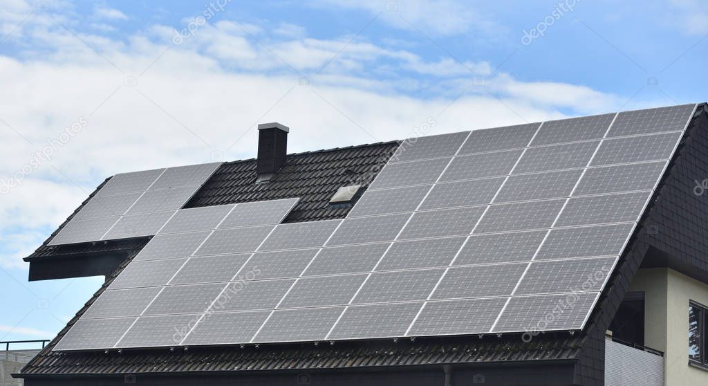 Solar panels installed on the roof of a house with tiles in Europe against the background of a blue sky.