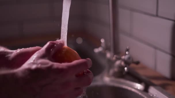 Мыть спелый апельсин под проточной водой на кухне, спрей крупным планом. Видео замедленного действия — стоковое видео
