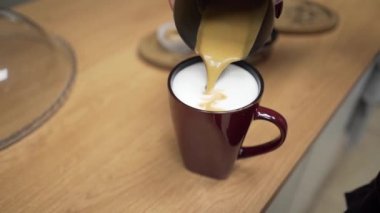 Barista kahve yapıyor ve sütlü bir fincana espresso döküyor. Bir resim oluşturuyor, yakın plan.