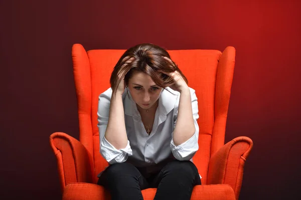 A stressed woman holds her head while sitting in a red chair during a coronavirus pandemic. The concept of viral danger, stress and fear