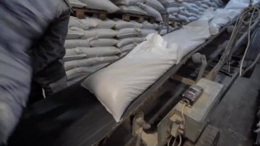 Bir adam taşıma bandına hayvan yemi torbaları koyar. Bir adam yem üretim fabrikasında çalışıyor.