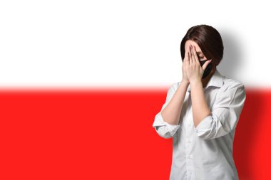 Stresli ve koruyucu maskeli bir kadın, ellerini Polonya bayrağının arka planına koyup yüzünü kapatıyor. Anksiyete ve korku kavramı, koronavirüs salgını COVID-19