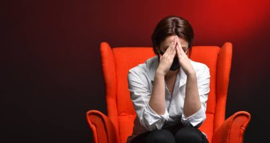 Stresli bir kadın, test ve koronavirüs salgını sırasında kırmızı bir sandalyede otururken başını tutar. Virüs tehlikesi ve korku kavramı