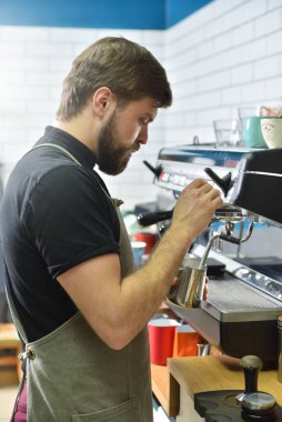 Sakallı bir barmen kahve makinesinde kahve yapıyor ve buharla süt çırpıyor..