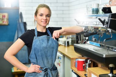 İşteki genç kız kahve makinesinin yanında duruyor ve gülümsüyor. Kahve dükkanında çalışan güzel sarışın kadın.