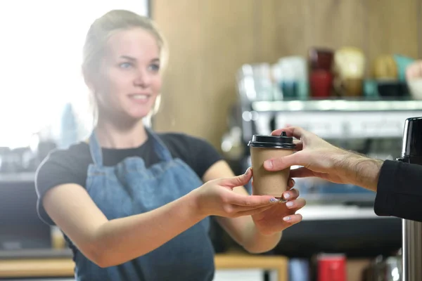 The bartender girl gives the customer coffee in a paper Cup, hands close-up.
