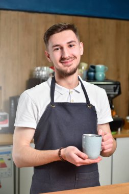 Elinde büyük bir fincan kahve tutan ve gülümseyen genç bir barista..