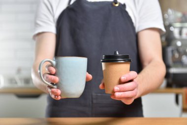Genç bir baristanın elinde bir kupa kahve ve paket kahvenin olduğu bir kağıt bardak var. Seçim ve Küçük İş Konsepti