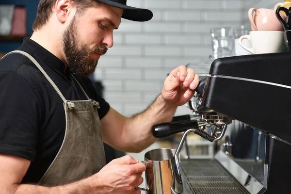 Bearded man barista making coffee on a coffee machine and whips milk with steam. Small business concept and sale coffee