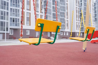 Çocuklar için yeni bir oyun parkında yeni bir apartmanın arka planında sallanmak.