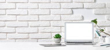 Beyaz masaüstü dizüstü bilgisayarı ve tableti olan beyaz tuğlalı bir duvarın arka planında kopya alanı olan.