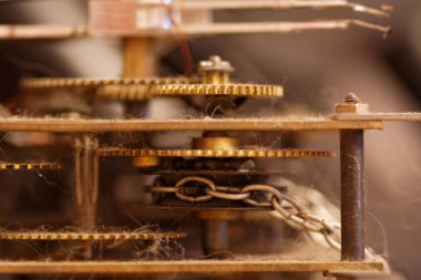 Eski bir duvar saatinin tozlu mekanizması zincir ve dişlilerle.