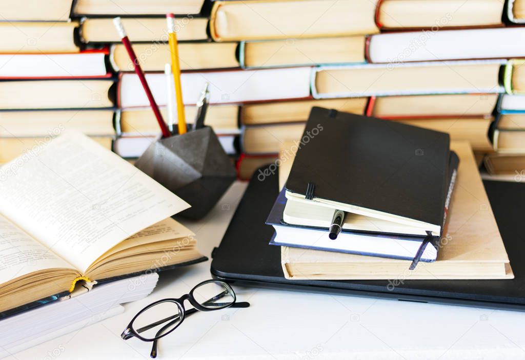 Stack of books, notebook, laptop, glasses in office background f